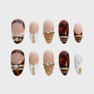 A set of press-on nails featuring tortoiseshell patterns, nude French tips, gold metal bands, and rhinestone details.