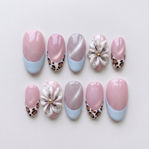 Pink cat-eye press-on nails with blue French tips, leopard print accents, and 3D white flowers.