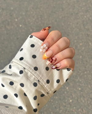 A set of press-on nails featuring tortoiseshell patterns, 3D white flowers, gold star charms, and yellow gradient details on a nude base.