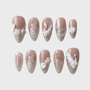 A set of press-on nails with 3D white roses, swan motifs, pearls, and rhinestones on a pearlescent nude base.