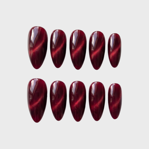 Ten almond-shaped press-on nails in a deep burgundy color with a magnetic cat eye shimmer effect.