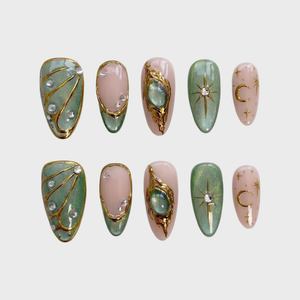 Sage green and pink press-on nails featuring gold celestial stars, crescent moons, butterfly wings, and rhinestone accents.