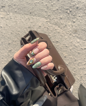 Sage green and pink press-on nails featuring gold celestial stars, crescent moons, butterfly wings, and rhinestone accents.