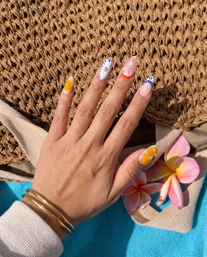 A set of press-on nails featuring 3D orange and pink fruit slices, blue floral patterns on white, and French tips.