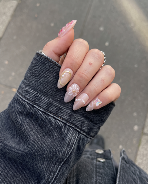 A set of pink press-on nails featuring 3D floral designs, iridescent butterfly charms, and gold wire accents.