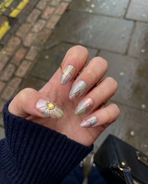 A set of iridescent press-on nails with gold kintsugi cracks and sunburst gemstone accents.