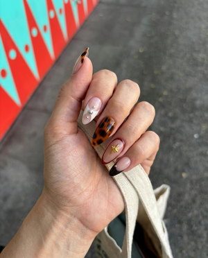 Tortoiseshell French tip press-on nails with gold star charms and silver studs.