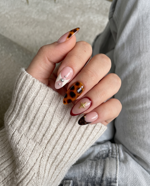 Tortoiseshell French tip press-on nails with gold star charms and silver studs.