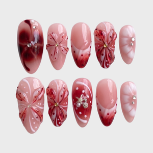 Set of press-on nails featuring red 3D floral designs, nautical charms, and rhinestone accents on a soft pink base.