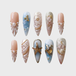 A set of stiletto press-on nails featuring ocean-themed designs with shells, pearls, starfish, and a sea turtle.