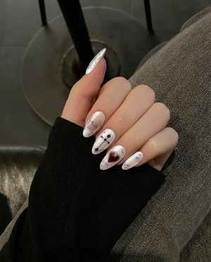 Pearl white press-on nails featuring metallic silver scrollwork, French tips, a dark red heart, and a gothic cross.