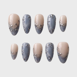 A set of press-on nails featuring a nude base, shimmering blue-grey French tips, and raised silver filigree swirl designs.