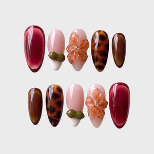 A set of press-on nails featuring burgundy cat-eye, tortoiseshell patterns, and 3D floral accents.