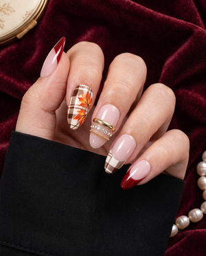 Pink and burgundy press-on nails with brown plaid, orange maple leaves, and gold accents