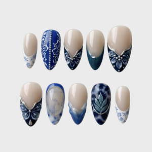 A set of blue and white porcelain-style press-on nails featuring floral patterns, marble designs, and silver accents.