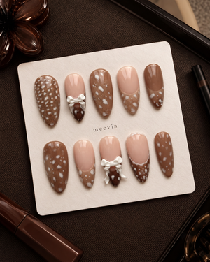 Brown and nude speckled press-on nails with raised white bow embellishments