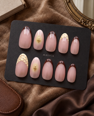 Glossy pink nude press-on nails with brown French tips, gold starburst accents, and cream floral details