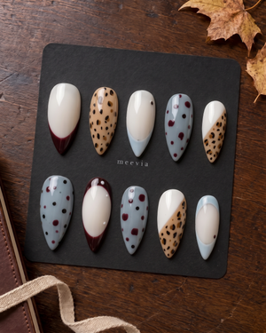 Glossy press-on nails with burgundy French tips, tan leopard print, creamy white bases, and blue dotted accents