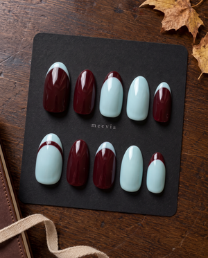 Burgundy and light blue glossy French tip press-on nails arranged on a black display board