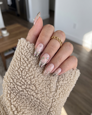 A set of pink press-on nails featuring gold metallic tips, celestial starburst details, and colorful iridescent gems.