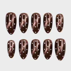 Almond shaped brown cat eye press-on nails with a white polka dot pattern.