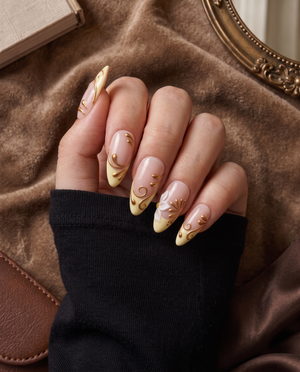 Glossy nude and cream press-on nails with white floral accents and raised gold swirls