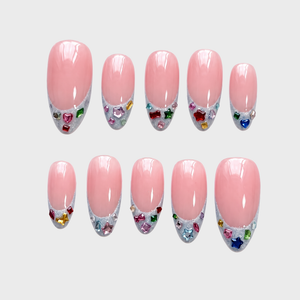 A set of pink French tip press-on nails decorated with colorful star and heart-shaped rhinestones.
