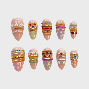 A set of ten nude press-on nails decorated with colorful rhinestones, gold chains, silver bands, white flower charms, and pastel patterns.