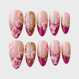 A set of magenta glitter French tip press-on nails decorated with 3D floral designs, gold filigree, and small white pearls.