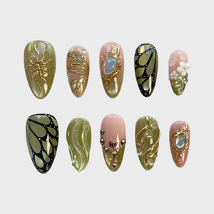 A set of press-on nails featuring olive green and pink bases decorated with gold butterfly wings, 3D flowers, and a large gemstone.