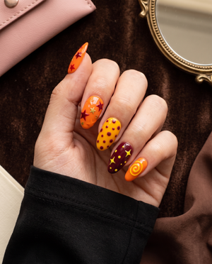 Orange and maroon celestial press-on nails with stars, dots, and swirl designs