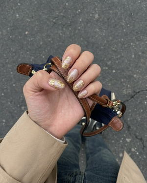 A set of oval press-on nails featuring a dusty pink shimmer base decorated with 3D metallic gold flowers and gold line accents.