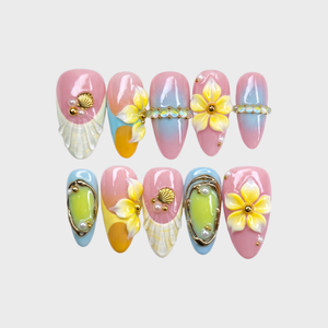 3D pastel press-on nails featuring yellow flowers, white seashells, gold accents, and a pink and blue gradient background.