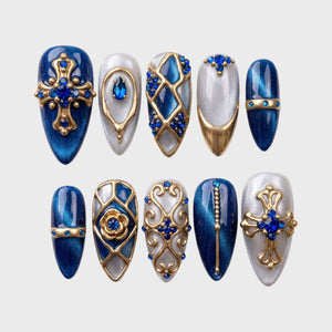 Royal blue and silver glitter press-on nails decorated with gold gothic crosses, baroque filigree, and blue rhinestones.
