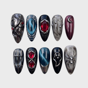 A set of gothic press-on nails featuring black, grey marble, and teal cat-eye bases with silver metallic spider, ghost, crescent moon, and red gemstone details.