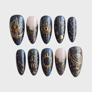 Celestial gold astrology press-on nails featuring sun, moon, and constellation designs on a dark pearlescent base.