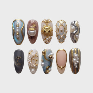Celestial themed press-on nails featuring gold sun, moon, and cauldron motifs adorned with pearls and gold beads.