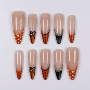 Stiletto press-on nails featuring orange french tips with polka dots, pumpkin vine motifs, and black tips with gold bead accents.
