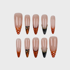 Stiletto press-on nails featuring orange french tips with polka dots, pumpkin vine motifs, and black tips with gold bead accents.
