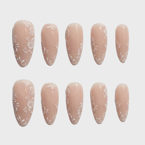 Almond shaped press-on nails in a nude color with white floral line art designs.