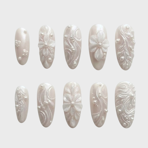 A set of pearlescent white press-on nails featuring 3D floral designs, raised swirls, and pearl embellishments.