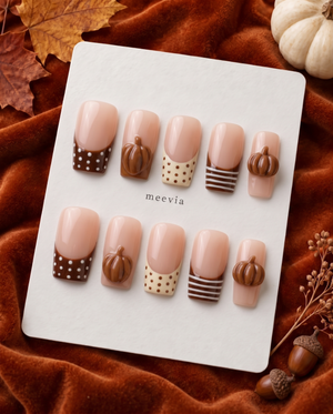 Glossy nude press-on nails with brown French tips, polka dots, stripes, and raised pumpkin accents