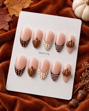 Glossy nude press-on nails with brown French tips, polka dots, stripes, and raised pumpkin accents