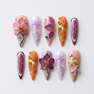 A set of stiletto-shaped press-on nails featuring 3D orchids, orange slices, fig patterns, and starfish embellishments.