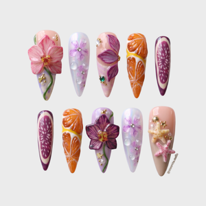 A set of stiletto-shaped press-on nails featuring 3D orchids, orange slices, fig patterns, and starfish embellishments.