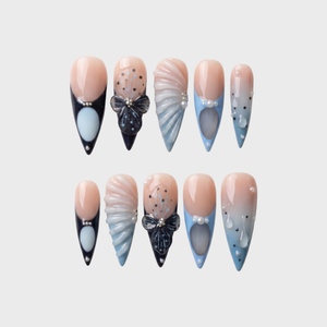 Set of stiletto press-on nails featuring blue and black French tips, butterfly art, pearl accents, and 3D shell textures.
