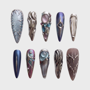A set of ten stiletto-shaped press-on nails with silver metallic liquid textures, celestial star designs, and embedded colorful gemstones.