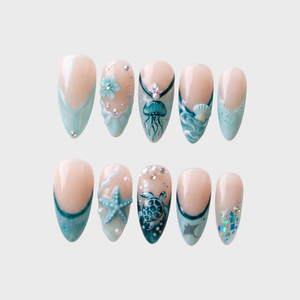 A set of teal-toned press-on nails featuring ocean motifs like a starfish, jellyfish, seashell, and sea turtle with rhinestone accents.