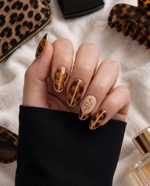 Glossy tortoiseshell press-on nails with gold edging, moon and star details, and a snake accent