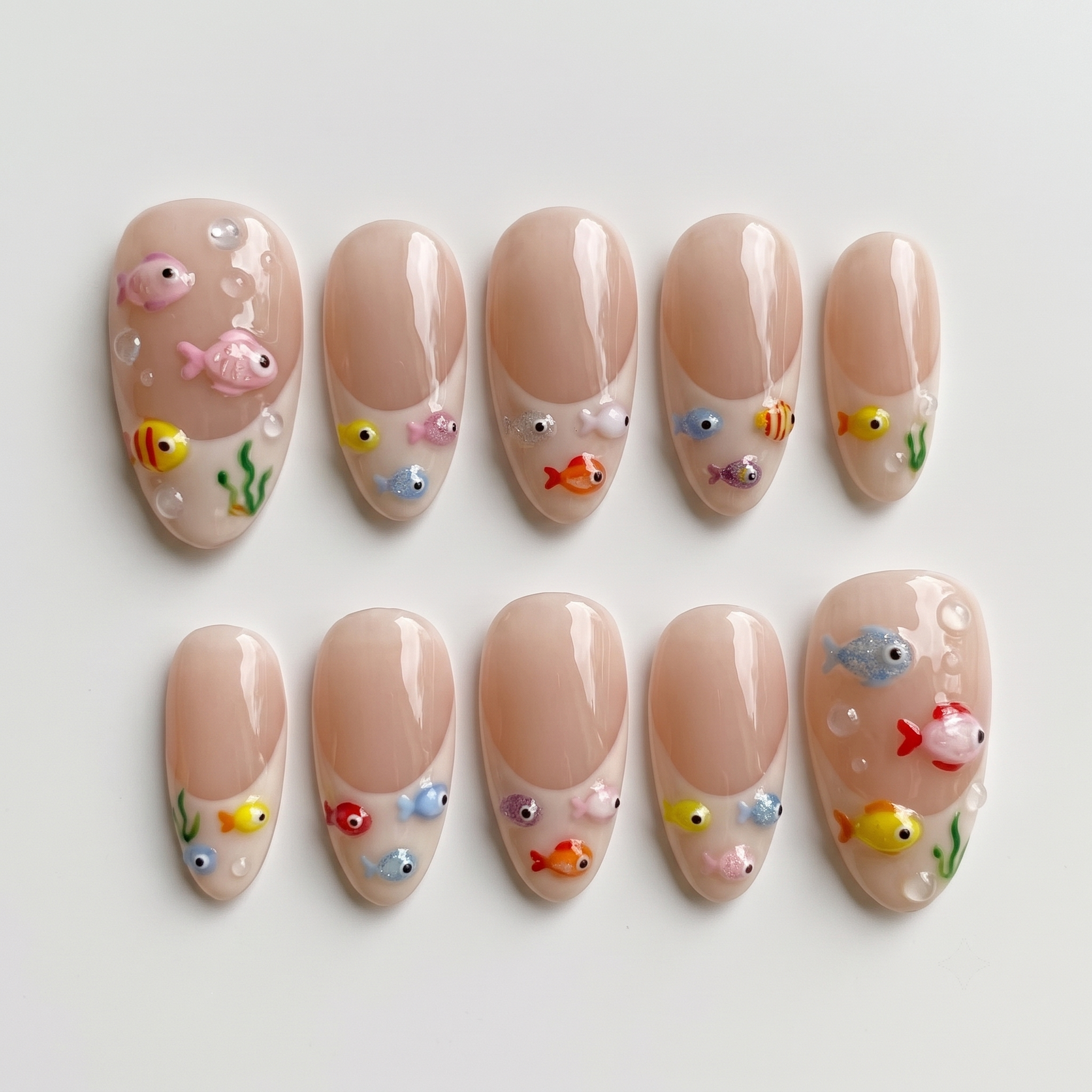 A set of nude French tip press-on nails decorated with 3D colorful fish, green seaweed, and clear water bubbles.